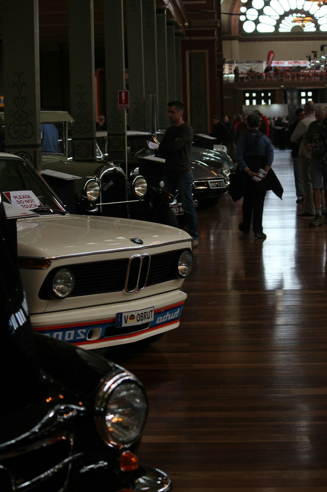 Elegant exhibition hall displaying rows of classic automobiles to visiting crowds